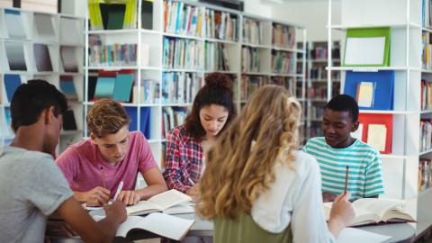 Group of teens studying at a table reading and writing