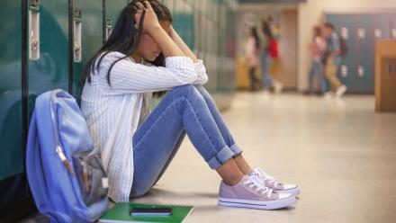 Middle grade student slouched against her locker with her hands in her hair and her knees pulled up.