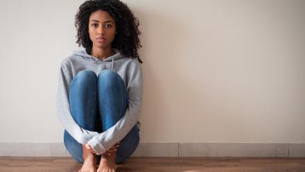 Young woman leaning against a blank wall hugging her legs.
