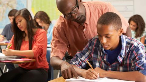 Black male high school teacher helping Black male student in class
