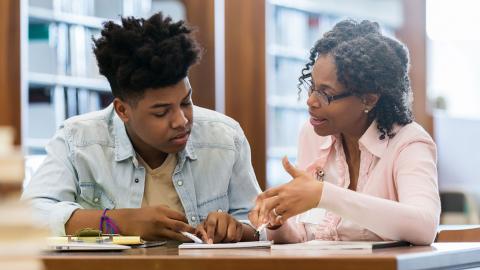 Black female tutor working one-on-one with Black male teen on school work