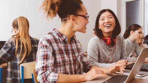 Mixed race teen girl and Asian teen girl working on writing in computer lab