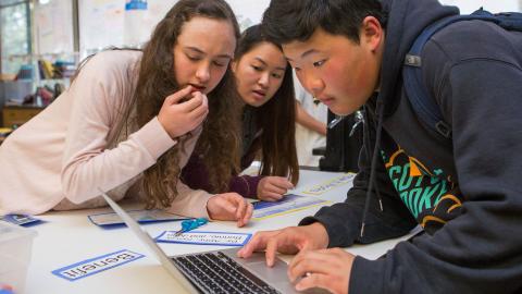Three multicultural high school students using laptops for class project