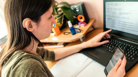 Teen girl with hearing aid working on laptop at home