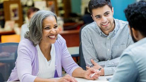 Older woman leading a conversation with younger, gentlemen colleagues