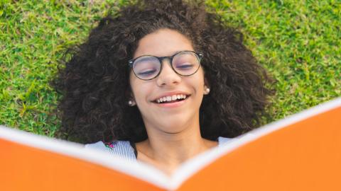 girl laying on grass reading an orange book