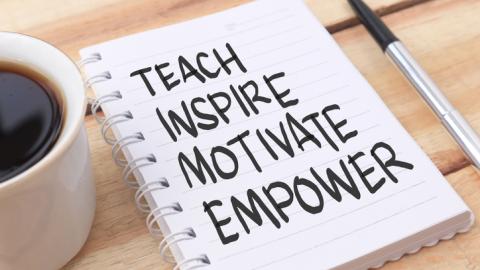 The words teach, inspire, motivate, and empower written on a notepad next to a pen and a cup of coffee