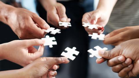 Seven peoples hand in a circle with white puzzle pieces