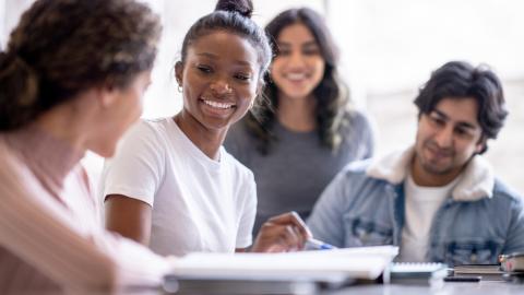 Group of teens sitting at a table and smiling while looking at their notebooks together