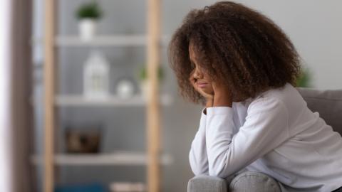 Adolescent girl looking sadly at the floor as she sits on a couch.