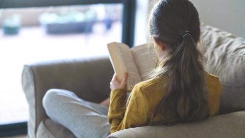 Teen girl reading on a couch not facing the camera