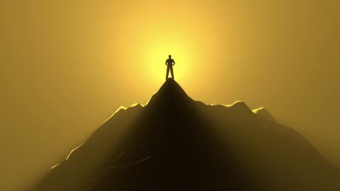 Person standing alone at the top of a mountain with the sun shining behind them.