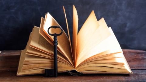 Large, old key laying against an open book sitting on a table.