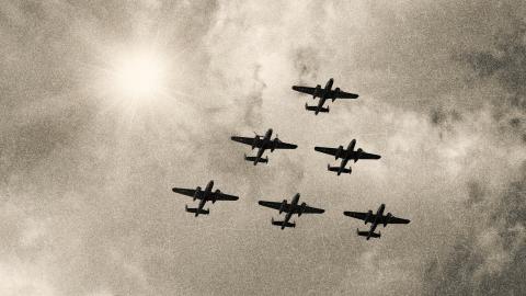Five WWII bomber planes flying through the sky in a triangle formation