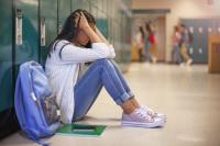 Middle grade student slouched against her locker with her hands in her hair and her knees pulled up.