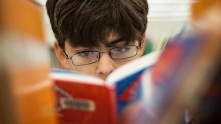 Looking through library book stacks at middle school boy reading a graphic novel