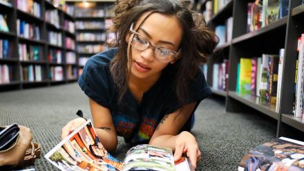 Mixed race high school girl laying on floor of library reading graphic novels