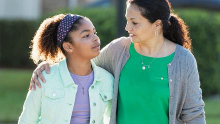 Mixed race mother with arm around tween daughter walking