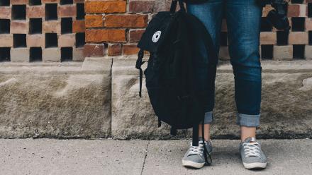 High school student wearing jeans and sneakers with backpack outside cropped from waist down
