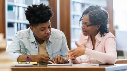 Black female tutor working one-on-one with Black male teen on school work