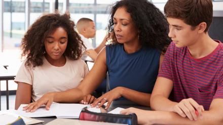 Multicultural teacher discussing reading with two high school students
