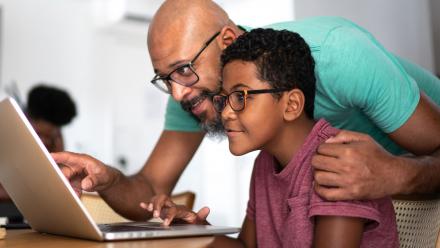 Father and middle school son looking at laptop together at home