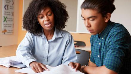 Black teacher working with Latino high school student on reading