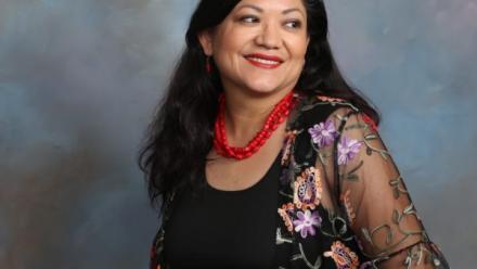 Picture of Reyna Grande looking to the side with a red, coral necklace and floral overlay wrap.