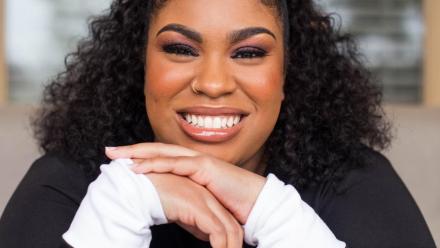 Author Angie Thomas smiling at the camera with her hands under her chin