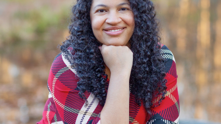 Michelle wearing a red, plaid dress smiling at the camera with her hand under her chin