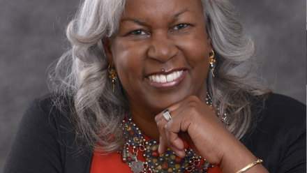 Sharon smiling to the camera with a hand under her chin