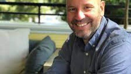 Chris Stevenson sitting on an outdoor couch, smiling to the camera