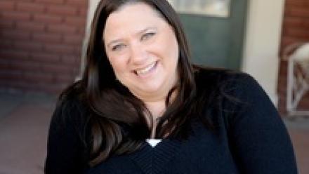 Head shot of Jennifer Brown in a black shirt sitting on the stoop of a brick house.