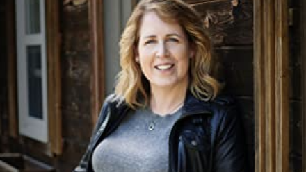 Author leaning against a window in a black jacket and jeans