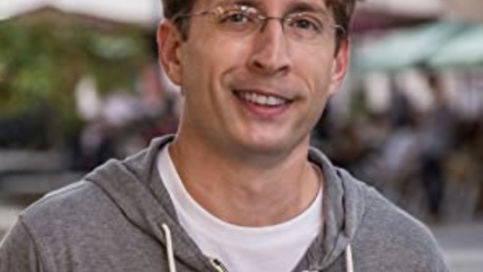 Headshot of Shaun wearing a grey hooded sweatshirt and glasses