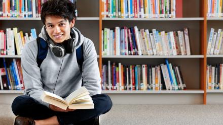Teenage boy reading a book sitting in a library