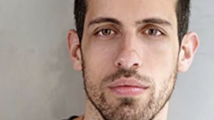 Adam looks into the camera for a head shot against a white wall.