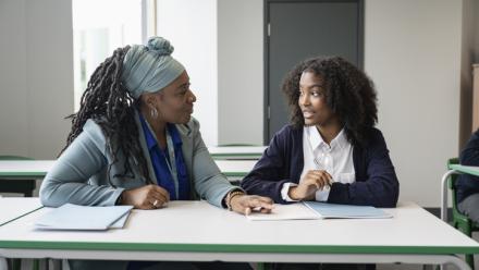 African American teacher and student sit at desks to discuss school work