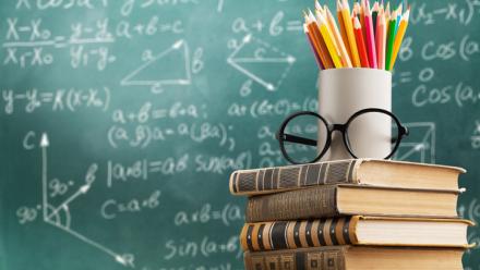 Math lesson on the chalkboard with books stacked in the front and colorful pencils stacked on top