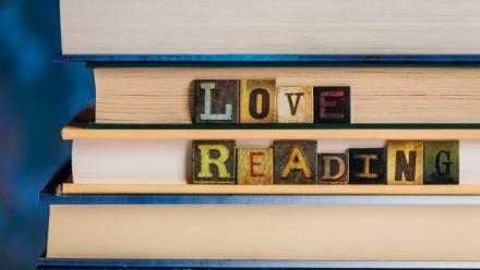 Books stacked with letter blocks spelling out "Love Reading" on the spine of the books