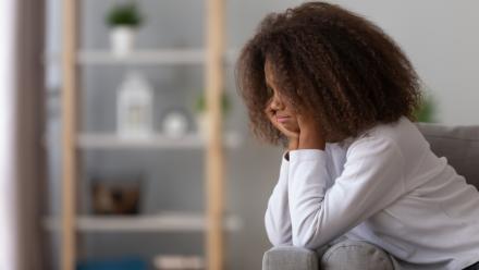 Adolescent girl looking sadly at the floor as she sits on a couch.
