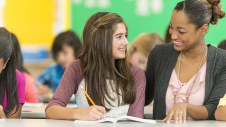 Teen and teacher smiling at one another as they sit together in the classroom