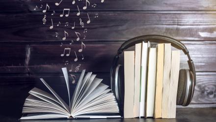 Book open with music notes floating above it, sitting next to a stack of books