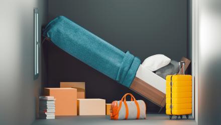 led leaning against a wall as it is too long to fit in the room; luggage is all over the floor of the room