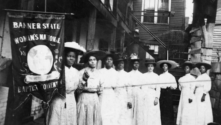 Suffragates from the early 1900's standing behind a banner.