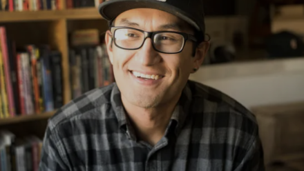 Head shot of illustrator Zeke Pena against a backdrop of books