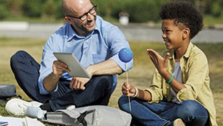 A male teacher sitting with a male student on the ground while learning