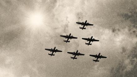 Five WWII bomber planes flying through the sky in a triangle formation