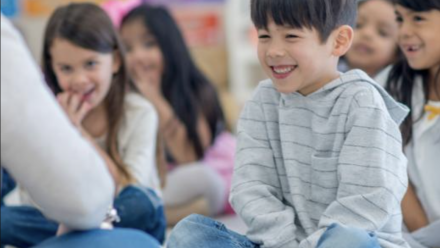 boy sitting on the floor in a classroom with other students and a teacher at the front