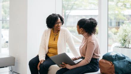 Two teachers speaking to one another while sitting on a bench.